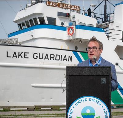 EPA Administrator Wheeler speaking at a lectern in front of the EPA research ship Lake Guardian.