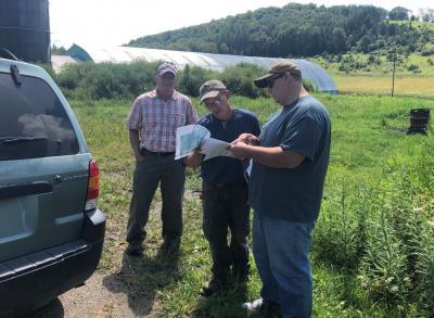 Three men standing in an agricultural field next to a truck and looking at a document together