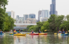 People kayaking on a river with a city skyline visible in the background.